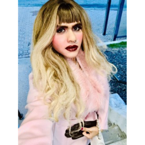 Crossdresser model wearing a pink coat, makeup and a pearl necklace.